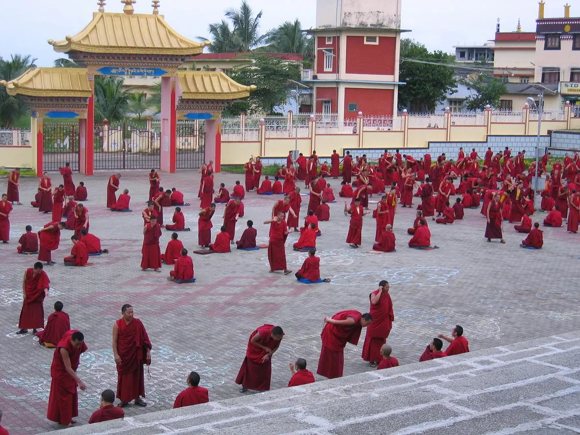 Hundreds of monks in maroon robes debating in pairs across the open courtyard at Sera, Bylakuppe