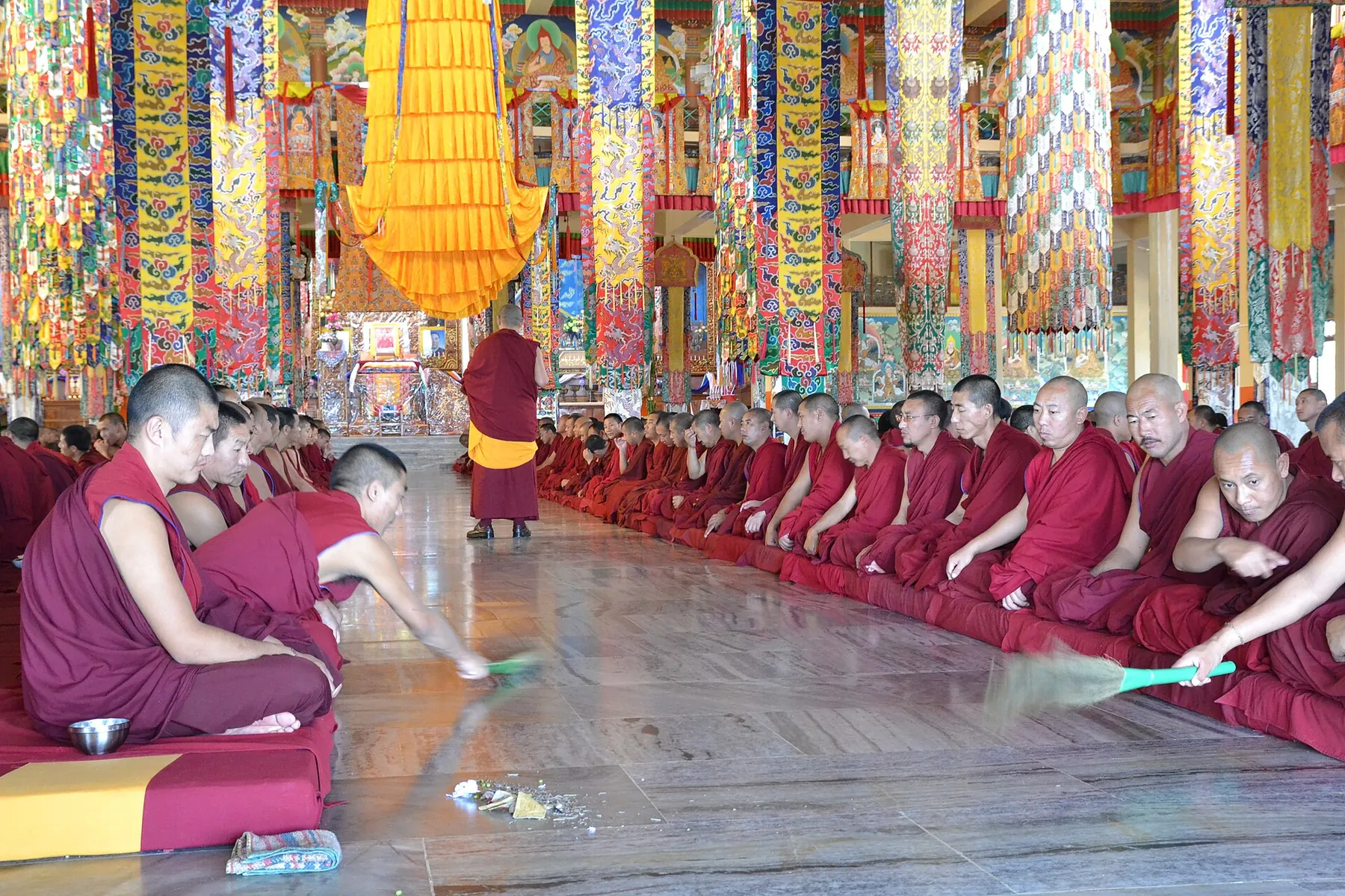 Monks seated in rows inside the richly painted great assembly hall during prayers